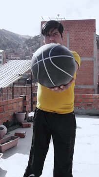 Vertical footage of a Hispanic guy playing with a ball on a rooftop