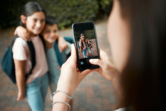 Children first day of school and mother taking photos with a phone of her cute kids. Closeup of screen picture of brother and sister embracing while posing for their mom outside in the morning