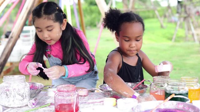 Lovely Asian and African girls playing dough together at playground, summer camp learning