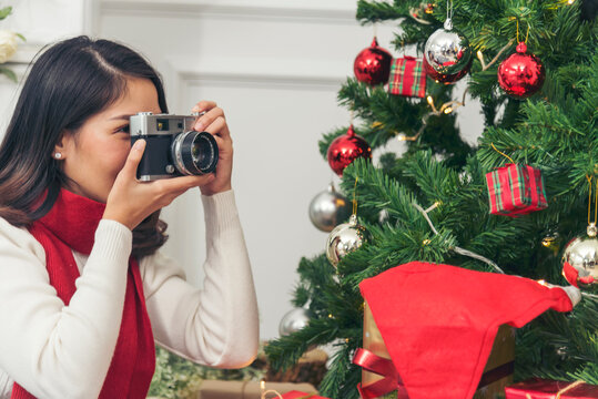 Woman Photographer take photo christmas decorate bauble ball xmas tree on holiday winter season celebrate. Asian woman using camera take photo christmas tree xmas present gift box in cozy living room