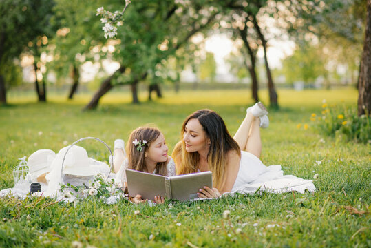 A mother and daughter in the spring garden on a plaid leaf through and look through a book with photos from a family photo shoot. Remember the important moments of life in the photo album.