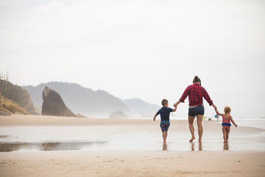 Rear view of mother walking on beach with her two young children.