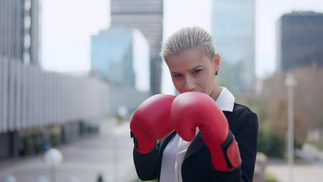 Businesswoman clashing boxing gloves and standing in guard position outdoors