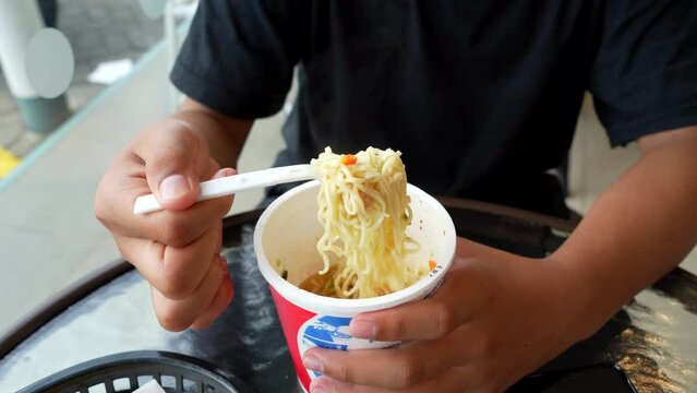 noodle soup in a cup, the boy stirs and feeds the noodles ready to eat