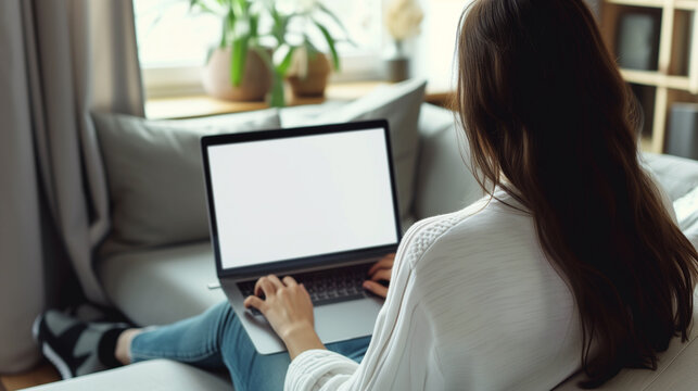 Mockup image of a woman working and typing on laptop computer with blank screen while sitting on sofa at home