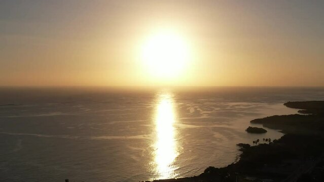 Drone footage of the bright sun in sunset sky and its reflection in the sea