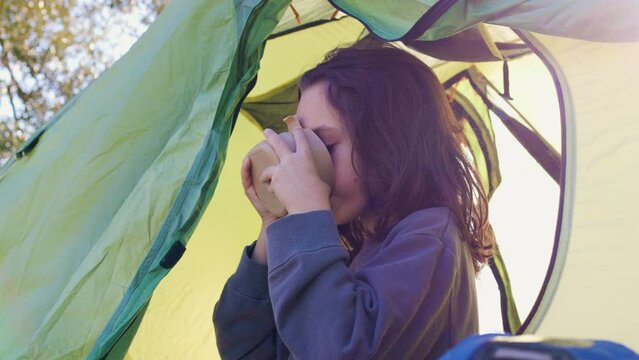 child sits in a tent and has breakfast. tent against the backdrop of the mountains. boy on a hike. boy in a sleeping bag with a plate in his hands. camping and trekking with children.