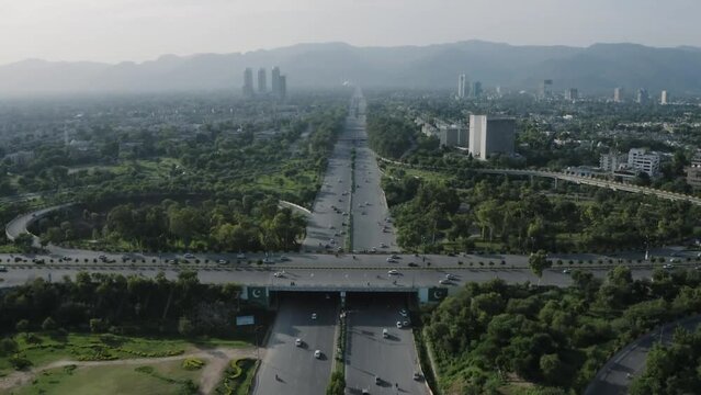 Road Traffic And Nature View From sky with drone camera. Bridge on Road for Road Crossing in Pakistan Islamabad. Pakistan Flag on Bridge. Trees and Nature beside the Road. Buildings and mountains 