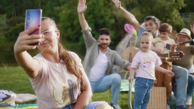 Adult woman taking a selfie photo on the phone with her multigenerational family on a summer camping trip in nature