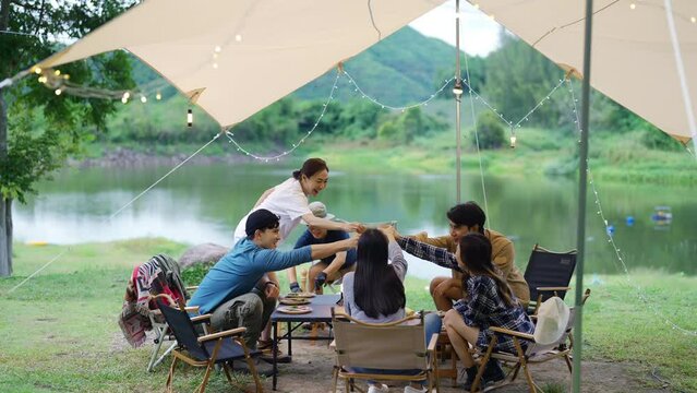 Group of Happy Asian man and woman enjoy and fun outdoor lifestyle travel nature camping in forest on summer vacation. People friends having dinner eating bbq grill and drinking beer together at night