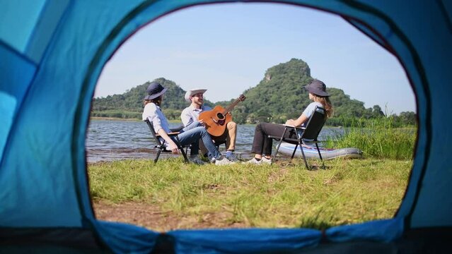 Group of travellers camping with friends they join drinking and playing guitar together with happiness activity camping near nature lake with mountain background is holiday summer camping concept.