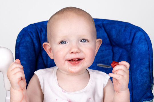 Cute little boy in a high chair eats fresh strawberries and smiles. White background. Close-up. Happy baby eating strawberries. Introduction of complementary foods, allergens. High quality photo