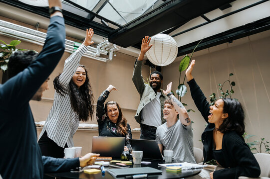 Group of cheerful male and female entrepreneurs celebrating after team meeting at office