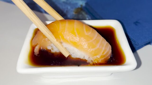 A close up view of a sushi roll being held with chopsticks and dipped into a mixture of soy sauce and wasabi sauce. Chinese food concept.