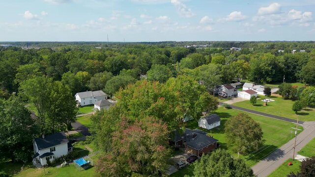 Aerial footage of a peaceful suburban neighborhood surrounded by lush green trees under a bright sky.