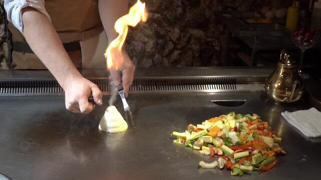 Chef's hand setting fire to a pyramid of chopped onions on a teppanyaki grill