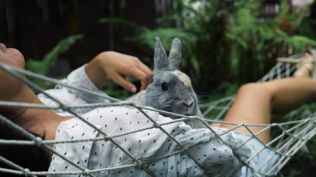 Asian girl lies on hammock in summer garden with Easter bunny. 