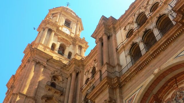 Low-angle shot of a historic cathedral tower in Málaga with detailed architecture, set against a clear, bright blue sky