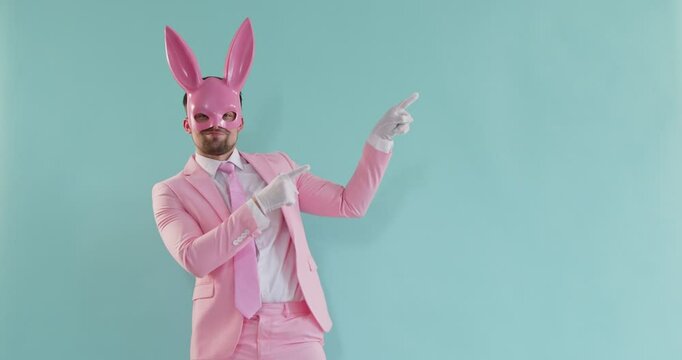 Funny man wearing pink rabbit, cute hare mask, formal beautiful pastel color suit, gloves finger pointing to show, dancing charming bunny animal representation love party show, sweet easter copy space