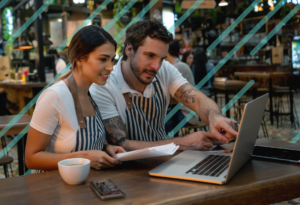 a man and woman both wearing aprons examine social media reporting for their restaurant