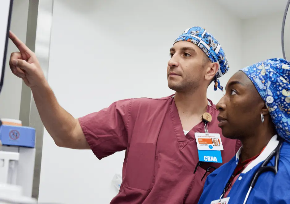 Two healthcare professionals wearing medical scrubs looking at a screen