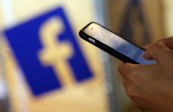 A visitor uses a mobile phone in front of the Facebook logo at the #CDUdigital conference.