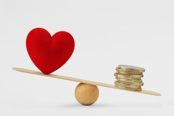 Heart and coins sit on opposite ends of a board balanced on a ball