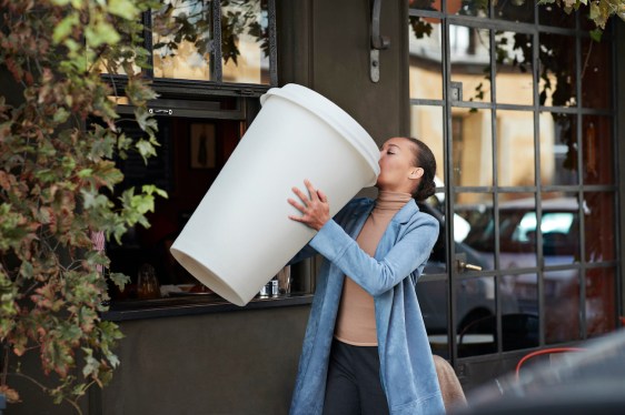 Young woman drinking coffee from large disposable cup at take away counter of cafe