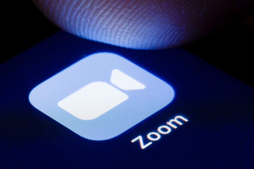 Finger poised above Zoom app icon on mobile phone.