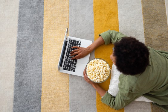 Top view of African American adult woman laying on ground and using laptop at home