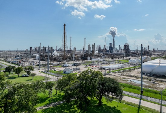 An oil refinery in the background across a lush green landscape with blue skies.