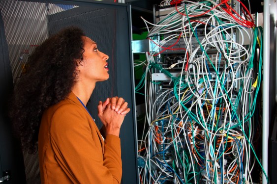 woman, pleading, standing in front of a tangled mass of computer cords and wires