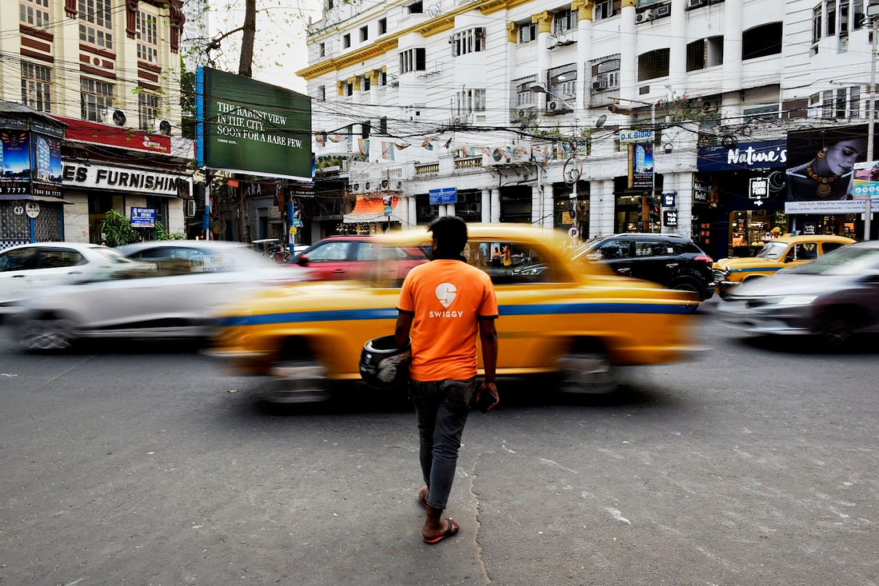 man in Swiggy shirt crossing heavily traffic on street