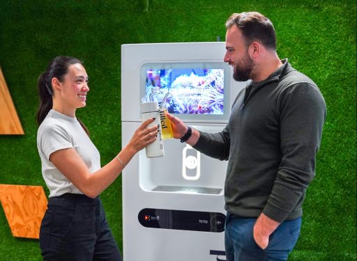 A photo of a woman and man standing with water bottles in front of a white Refiller drink dispenser