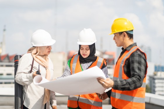 Two women and a man in construction gear looking at a blueprint on a job site