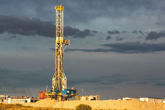 A rig drills into the earth against a cloudy sky.