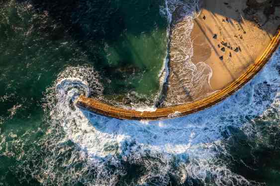 Aerial photo of Children's Pool La Jolla facing giant waves during the king tide event while the seals are sleeping on the beach in the sunny San Diego California