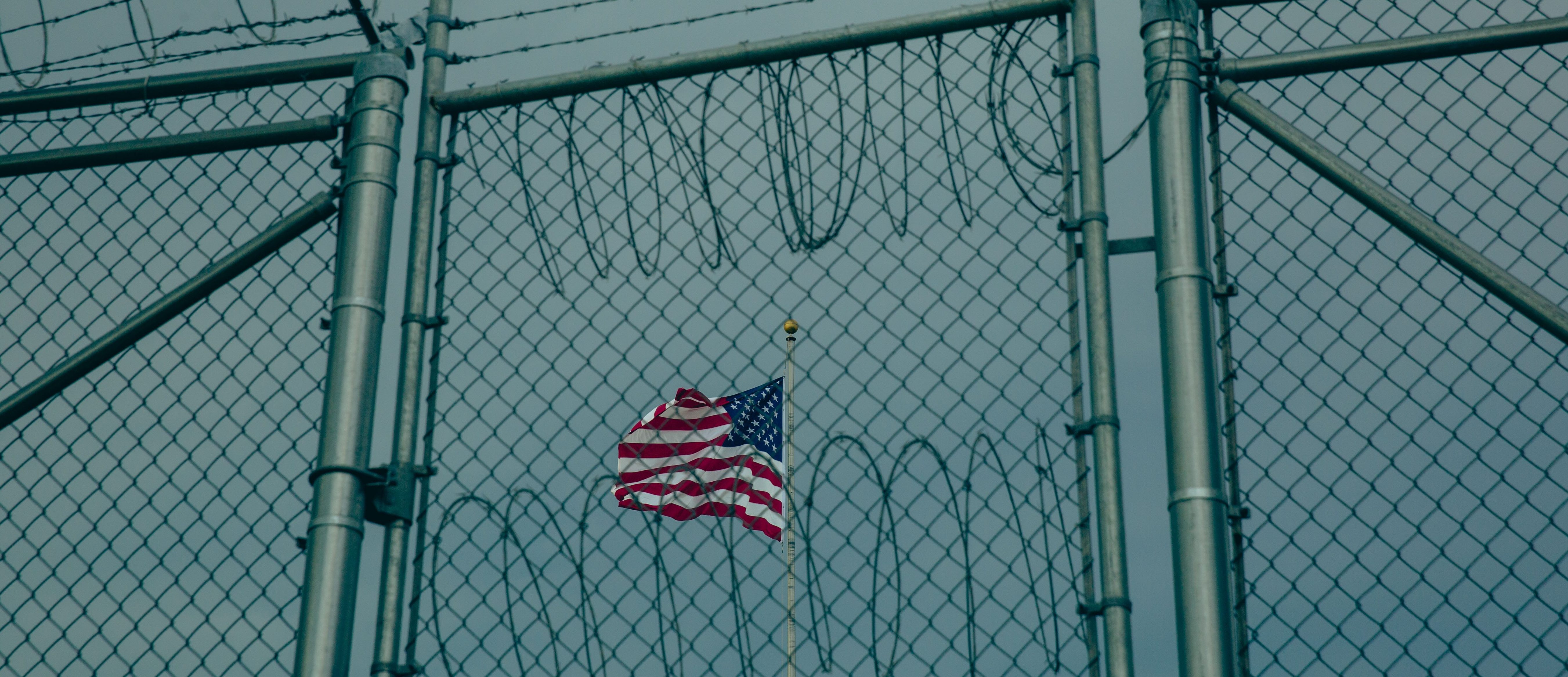 GUANTANAMO BAY, CUBA - JUNE 27: (EDITORS NOTE: Image has been reviewed by the U.S. Military prior to transmission.)  An American flag flies behind barbed wire fencing at the Office of Military Commissions building on June 27, 2023 at Guantanamo Bay, Cuba. At the prison within Naval Station Guantanamo Bay where media members are no longer allowed, 30 men still remain imprisoned while five separate war crime prosecutions involving some of the detainees proceed within Guantanamo's war court  none have yet reached a trial date. (Photo by Elise Swain/Getty Images)