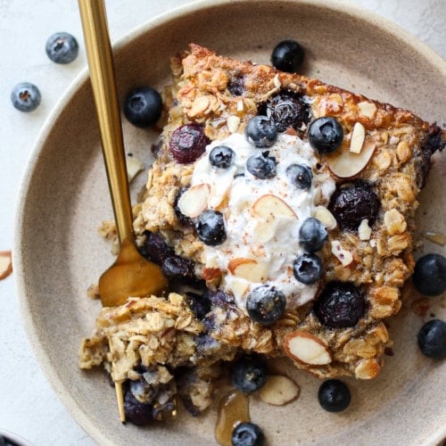 Serving of healthy blueberry baked oatmeal in stone shallow bowl, topped with yogurt and fresh blueberries.