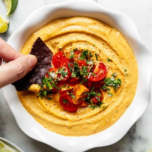 Creamy vegan nacho queso dip being dipped out with a blue corn chip