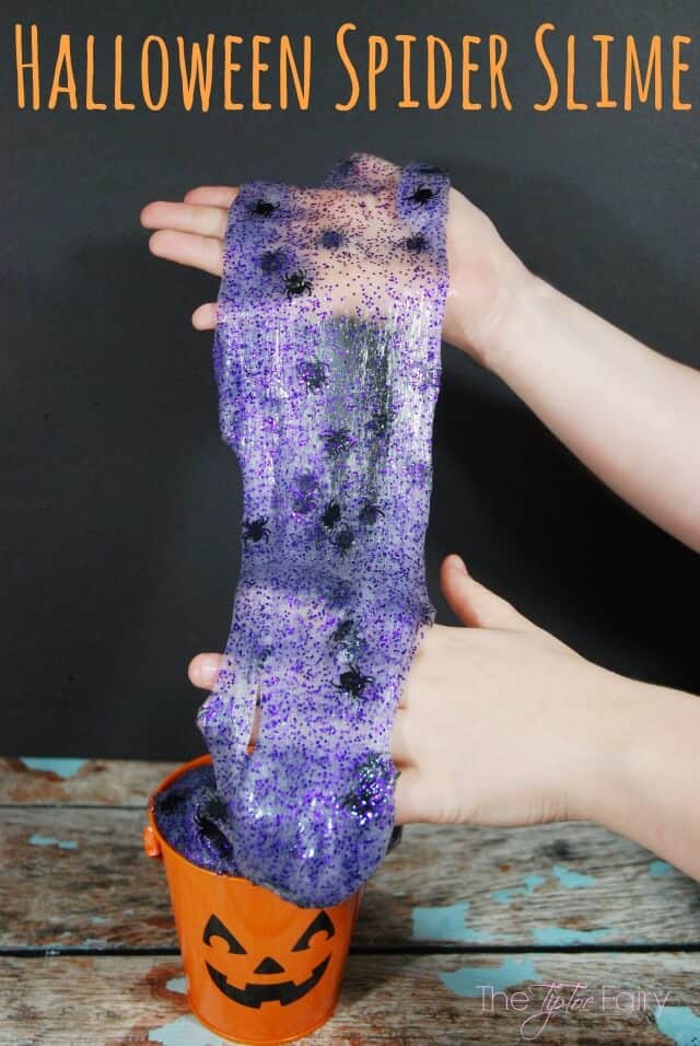 Purple slime with glitter and plastic spiders in it being pulled up and stretched out of a pumpkin pail.