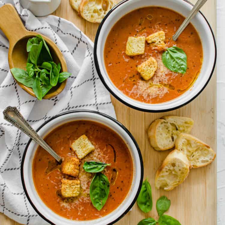 Tomato bisque in bowls with spoons and croutons on top.