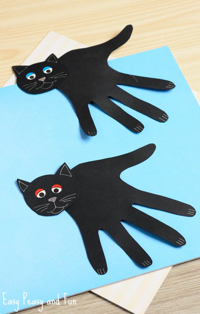 Black cats made out of construction paper hand print cutouts.