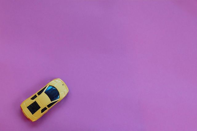 Yellow toy car on purple background viewed from above, offering a minimalist and creative feel. Suitable for use in children's toy advertisements, playful promotional materials, educational content, or automotive-themed graphics.