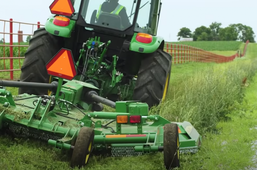 Rotary cutting between a fence and a gravel road.