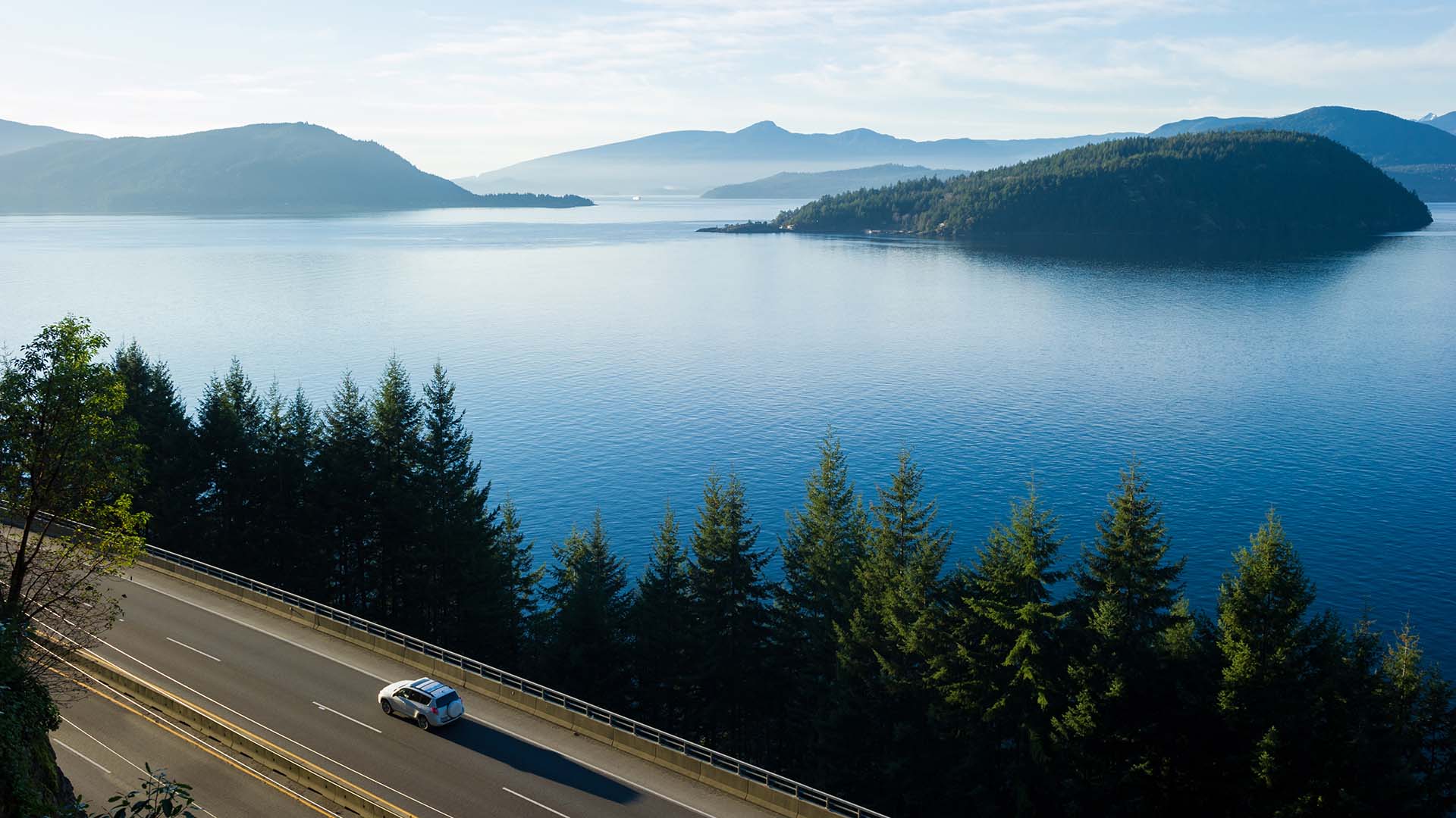 Car driving down highway 99 next to lakes and mountains with fog in the background.