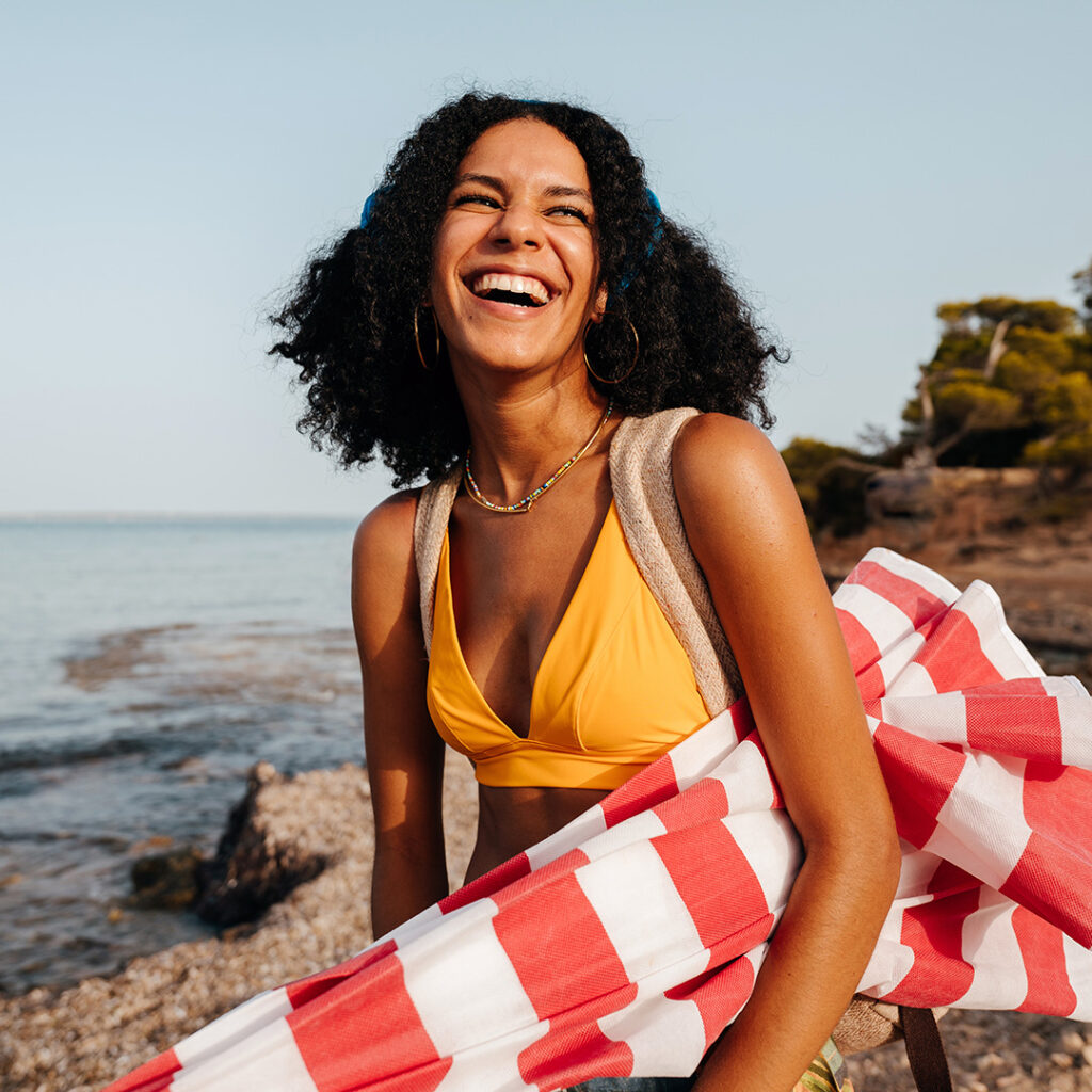 woman in yellow bathing suit, holding beach umbrella on rocky shore