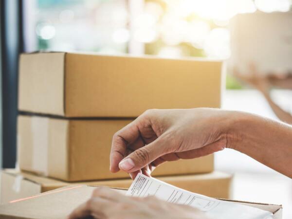 An eBay seller applying a shipping label to a package with 3 packages stacked behind the box.