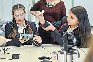 Teaching Secondary Science: young girls using science technology in a classroom as a teacher observes