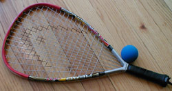 Racquetball A racquet sport played with a hollow rubber ball in an indoor or outdoor court.